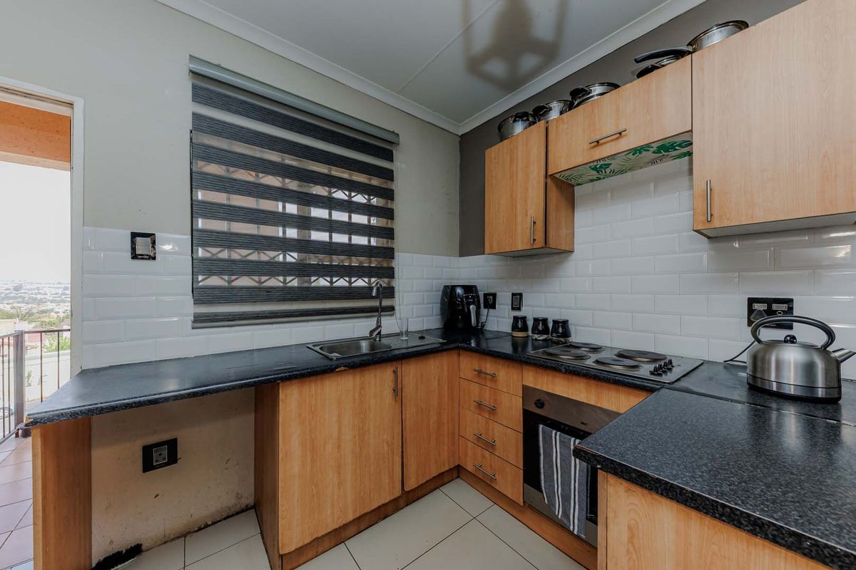 A functional kitchen featuring light wood cabinetry, dark laminate countertops, subway tile backsplash, and integrated cooking appliances with direct access to an outdoor balcony.