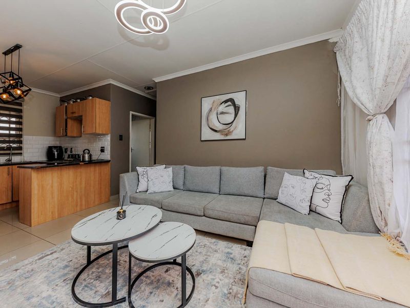 An open-plan living area featuring a compact kitchen with wood-finish cabinetry, subway tile backsplash, and modern lighting, seamlessly connected to the lounge space.