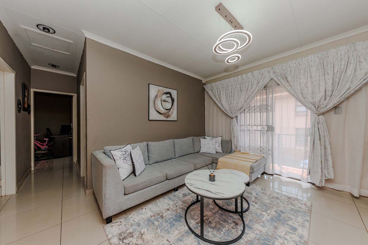 A well-maintained living room featuring tiled flooring, a modern pendant light fixture, and a sliding glass door leading to an outdoor area.