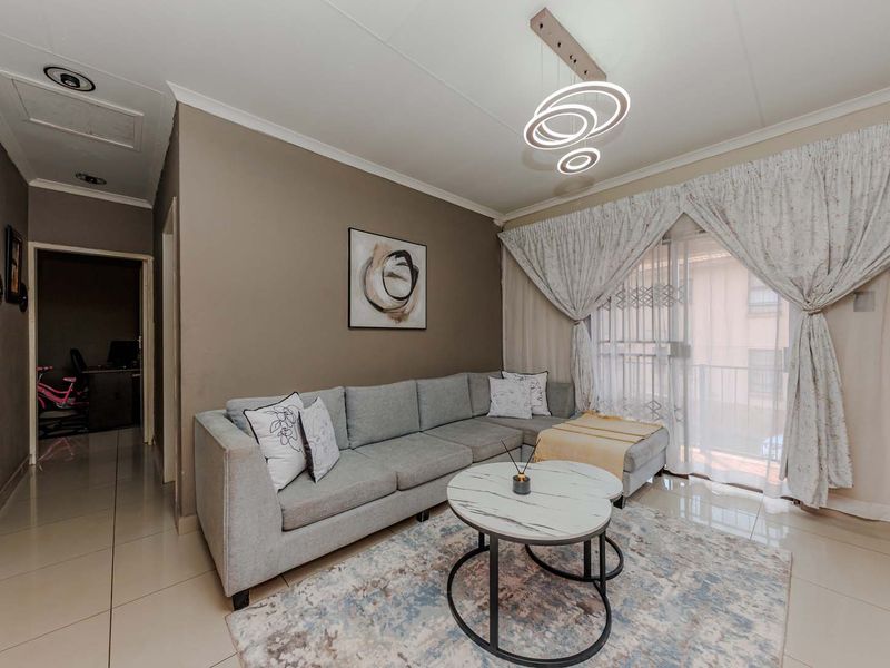 A well-maintained living room featuring tiled flooring, a modern pendant light fixture, and a sliding glass door leading to an outdoor area.