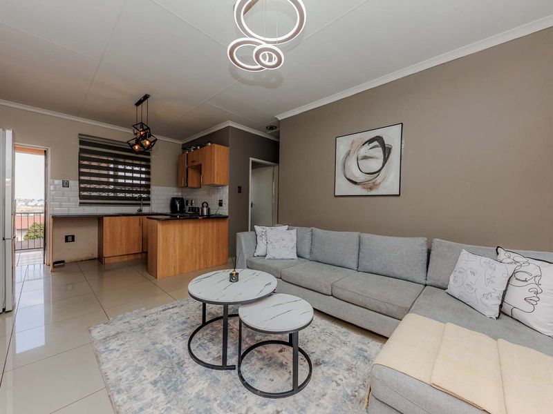 Open-plan living area featuring a functional kitchen with subway tile backsplash, tiled flooring, and modern lighting fixtures, leading to an exterior balcony.