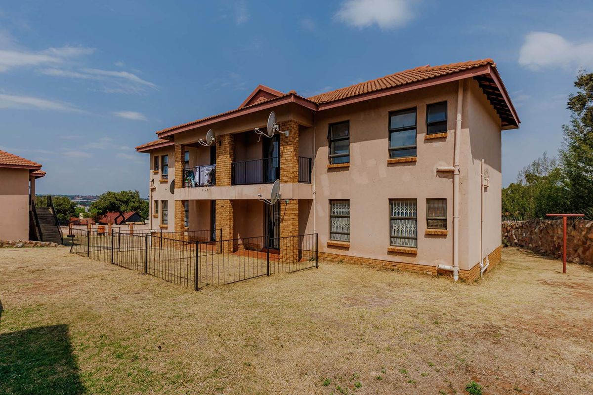 Rear view of a two-story townhouse featuring a balcony, brick accents, security window bars, and a private fenced garden area.