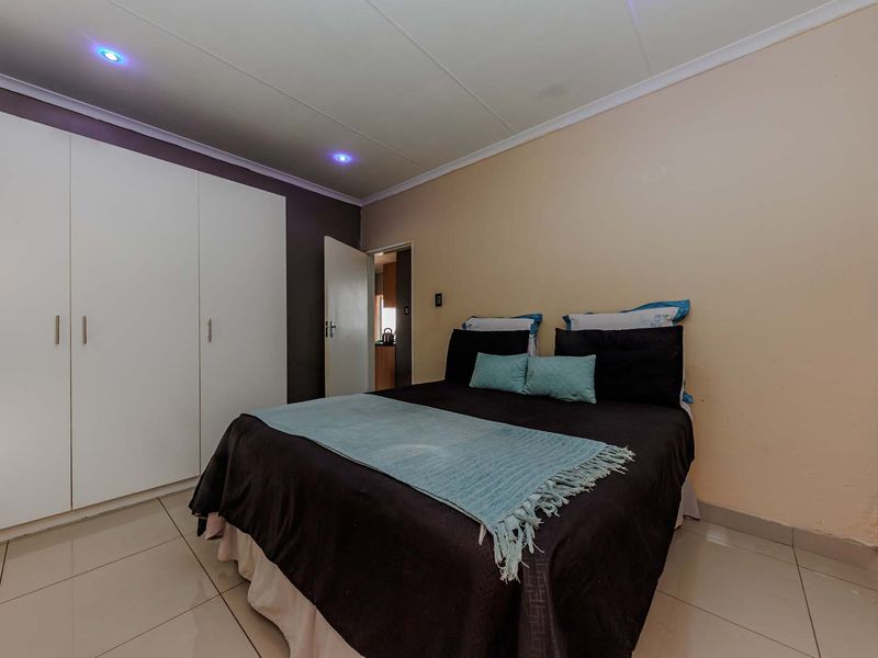 A bedroom featuring built-in cupboards, tiled flooring, and recessed downlighting, offering a functional space with neutral wall finishes.