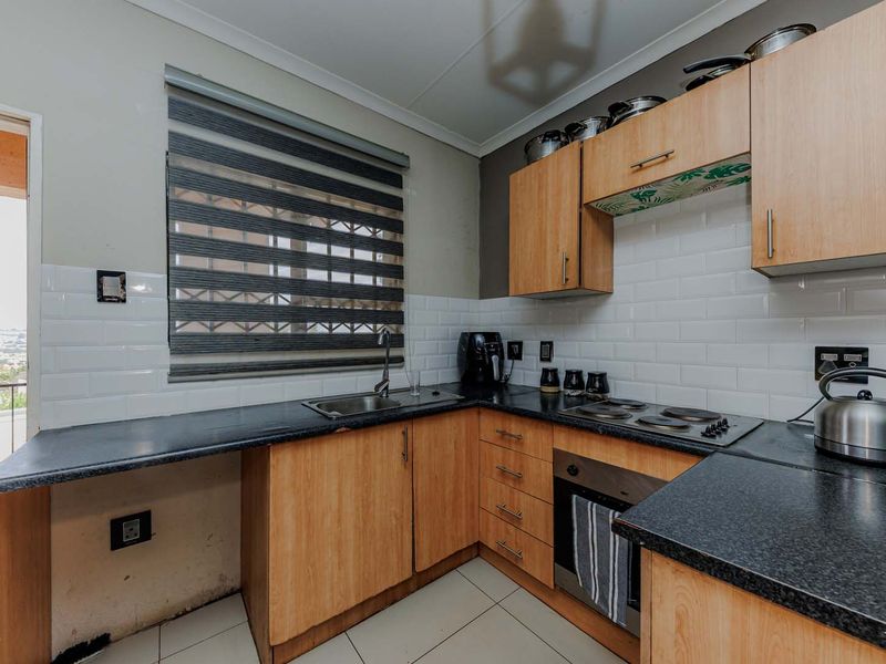 A functional kitchen featuring light wood cabinetry, dark laminate countertops, subway tile backsplash, and integrated cooking appliances with direct access to an outdoor balcony.