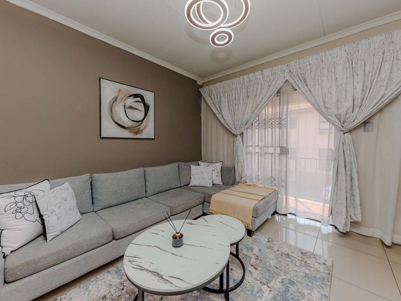 A well-maintained living room featuring tiled flooring, a modern pendant light, and a sliding glass door with security gate leading to a balcony.