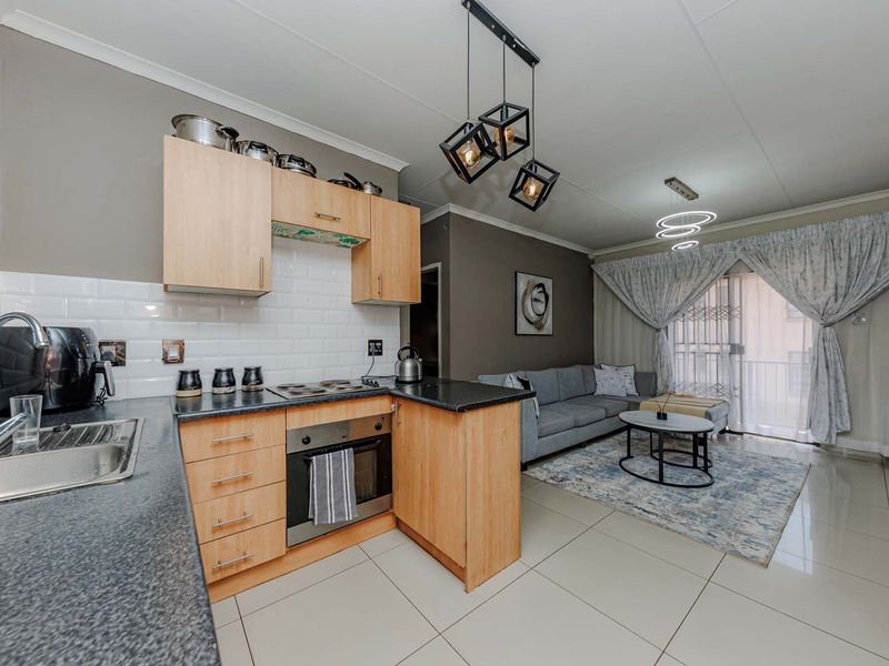 Open-plan living area featuring a functional kitchen with light wood cabinetry, subway tile backsplash, and direct access to a balcony through sliding glass doors.