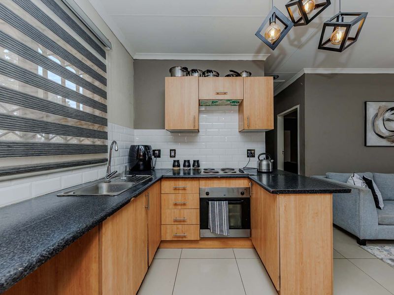 Open-plan kitchen featuring light wood cabinetry, dark laminate countertops, subway tile backsplash, and integrated oven with hob, flowing into the living area.