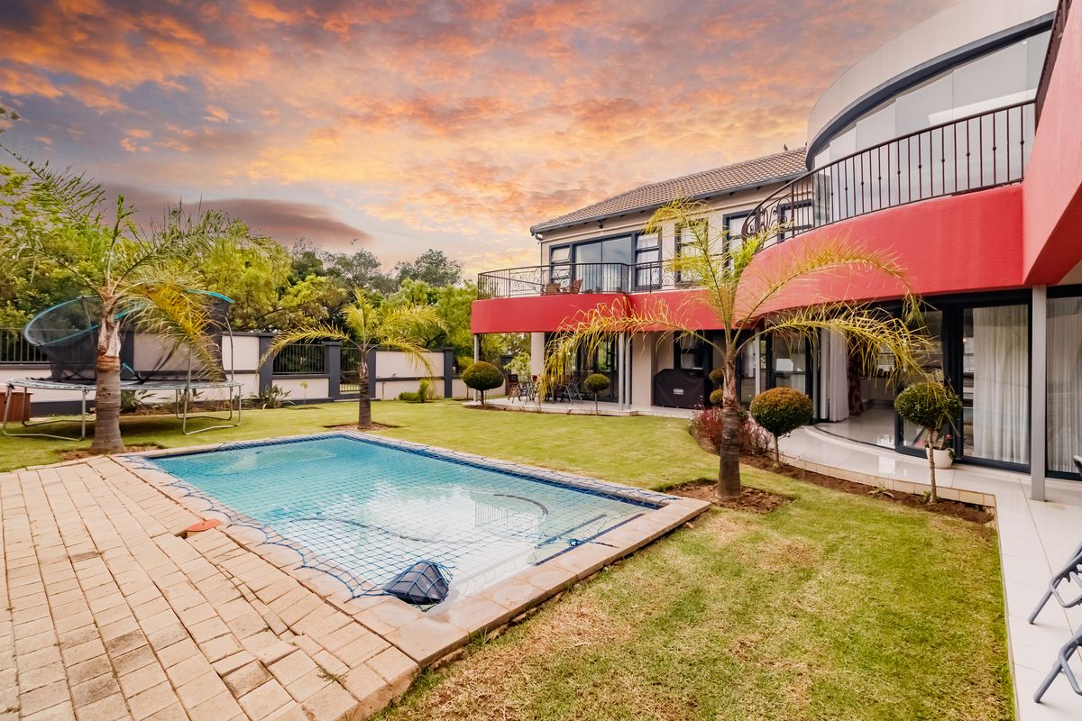 A spacious rear garden featuring a swimming pool with safety net, manicured lawn, and a large upper-level balcony with wrought iron railings.