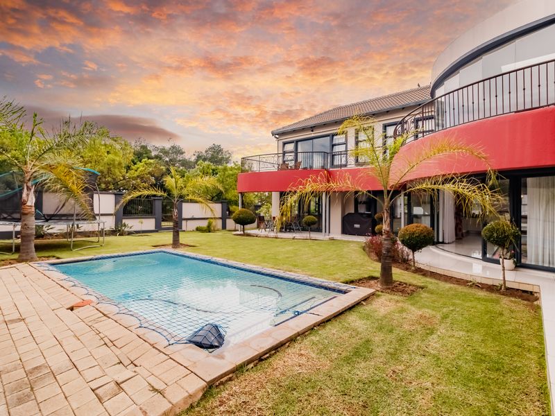 A spacious rear garden featuring a swimming pool with safety net, manicured lawn, and a large upper-level balcony with wrought iron railings.