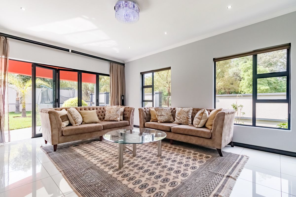 A bright and spacious living room featuring large aluminium-framed windows, sliding doors to the garden, polished porcelain tiles, and elegant recessed lighting.