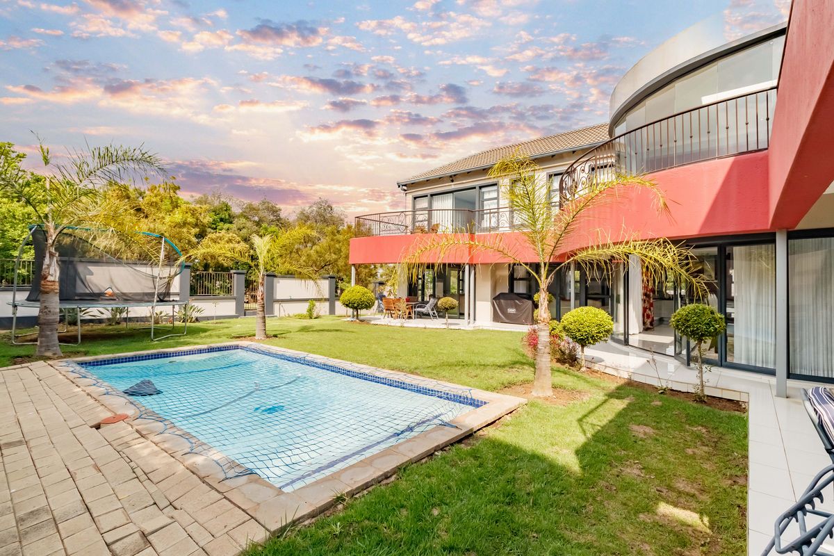 Rear view of the property featuring a swimming pool, landscaped garden, paved patio area, and an upper-level balcony with wrought iron railings.