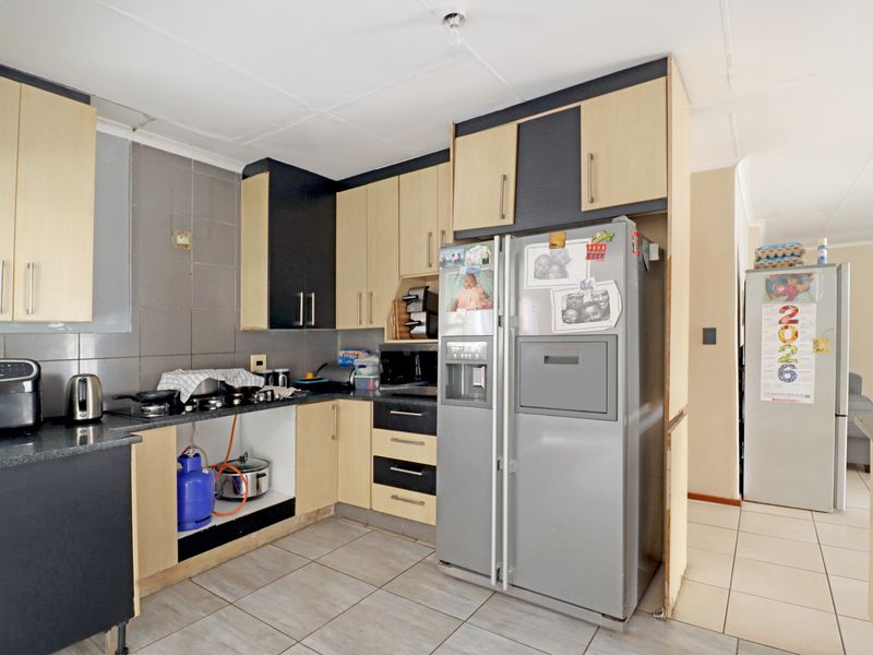 A functional kitchen featuring laminate cabinetry, granite countertops, and tiled flooring, currently requiring minor repairs and cosmetic updates to improve its overall finish.