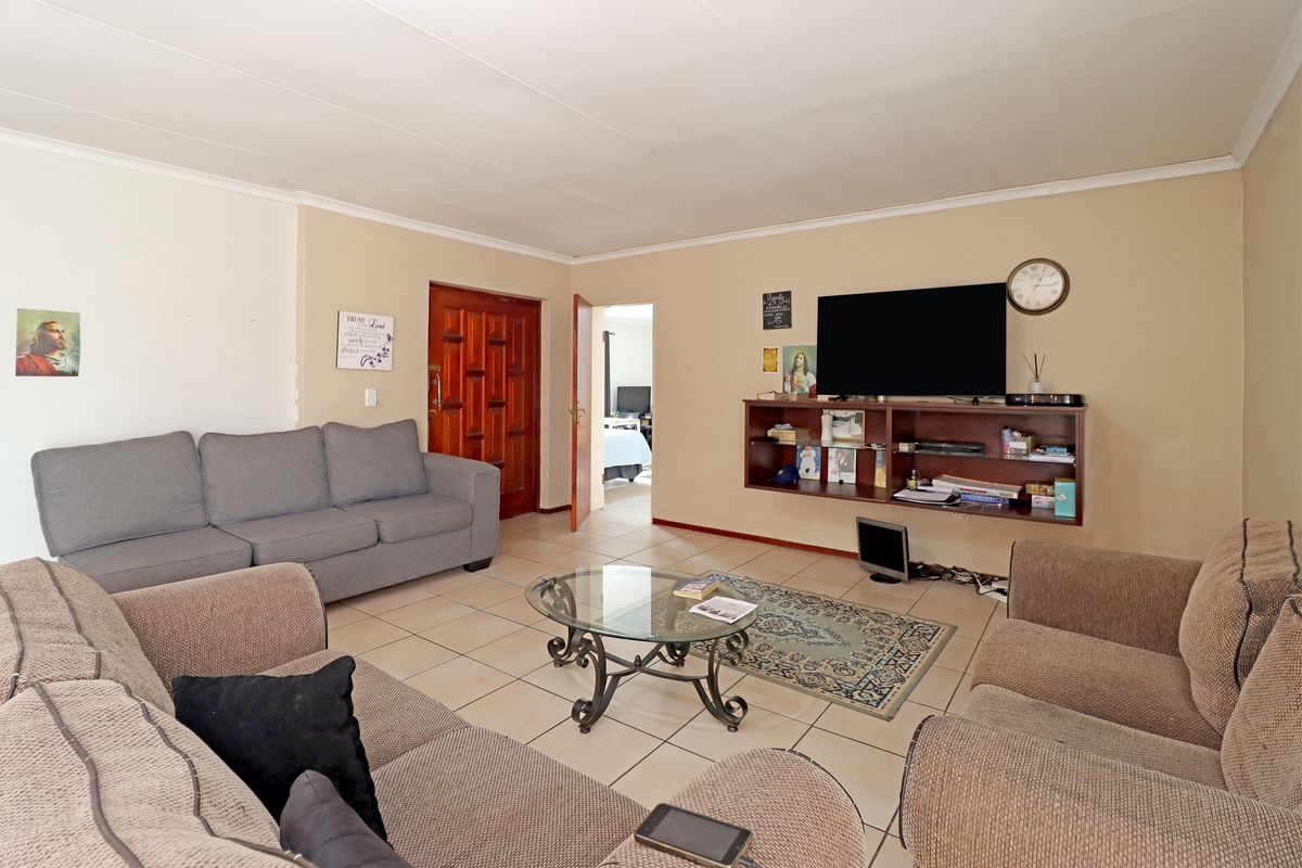 A spacious living room featuring neutral tiled flooring, a timber entrance door, and a wall-mounted shelving unit, offering a functional and comfortable living space.