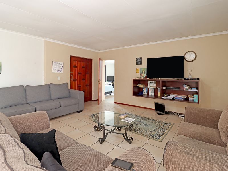 A spacious living room featuring neutral tiled flooring, a timber entrance door, and a wall-mounted shelving unit, offering a functional and comfortable living space.
