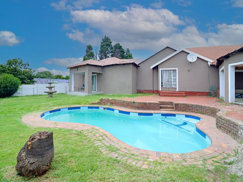 Rear view of the property featuring a swimming pool with brick surround, a retaining wall, and a covered patio area.
