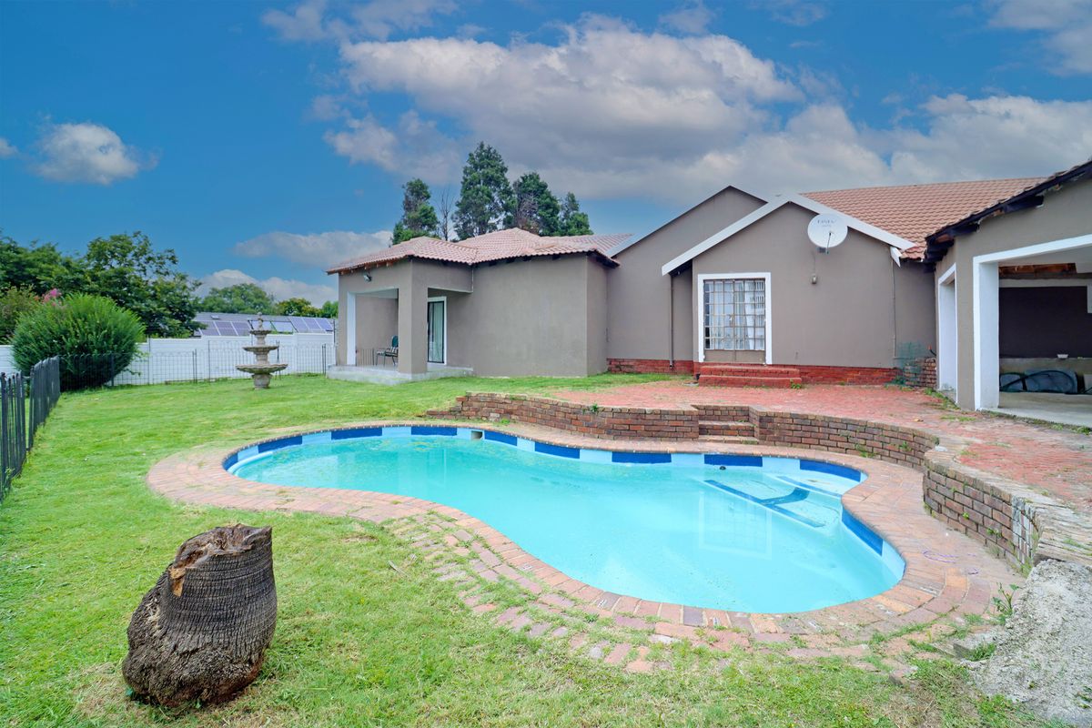 Rear view of the property featuring a swimming pool with brick surround, a retaining wall, and a covered patio area.