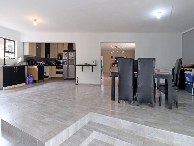 Spacious open-plan living and kitchen area featuring tiled flooring, built-in cabinetry, and a raised dining section.