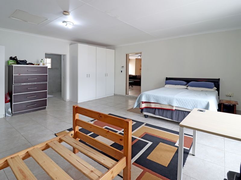 Spacious bedroom featuring neutral tiled flooring, ample built-in cupboard storage, and direct access to an adjoining room.