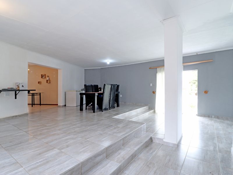 Spacious open-plan living area featuring light-toned tiled flooring, a raised platform section, and a structural column, leading to an outdoor access point.