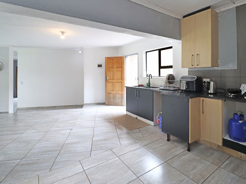 Open-plan living and kitchen area featuring tiled flooring, modern two-tone cabinetry, and direct access to an exterior door.