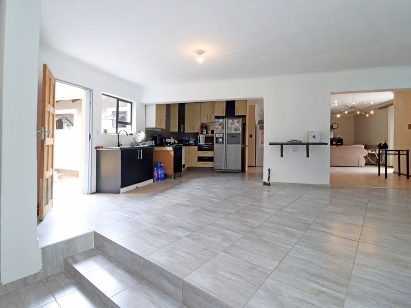Spacious open-plan kitchen and living area featuring tiled flooring, a raised floor section, and functional built-in cabinetry with direct outdoor access.