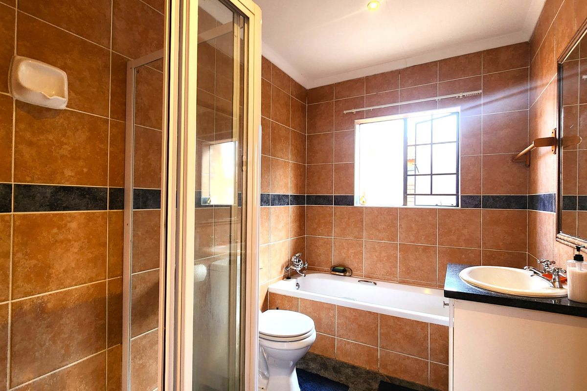 A functional bathroom featuring a shower enclosure, bathtub, vanity with basin, and toilet, finished with full-height wall tiling.