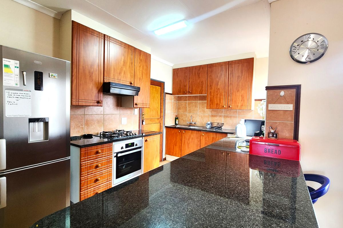 A functional kitchen featuring wooden cabinetry, granite countertops, a gas hob, built-in oven, and a tiled backsplash.
