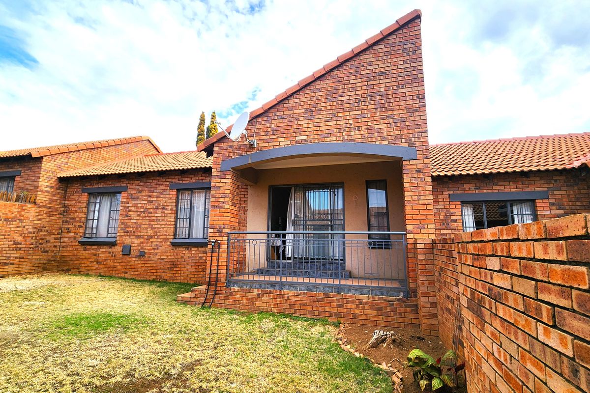 Rear view of a face brick townhouse featuring a covered patio, metal security gate, and a private garden area.
