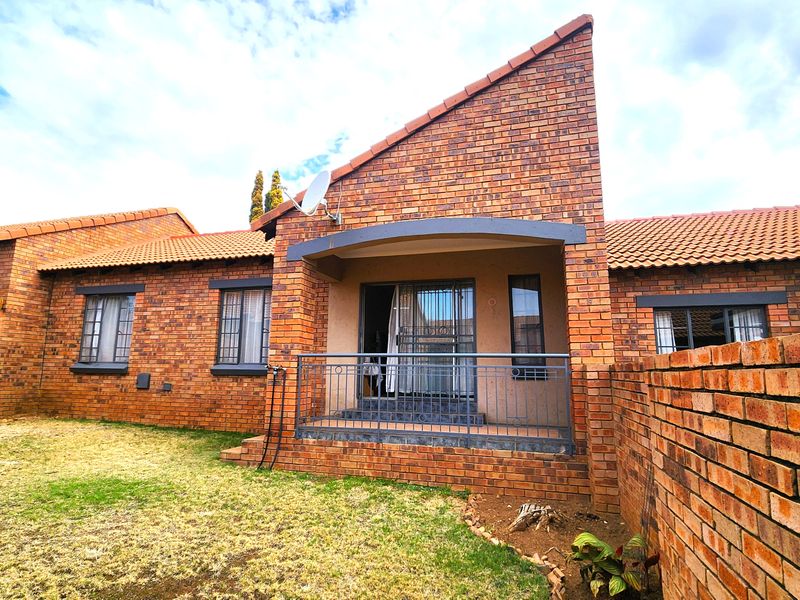 Rear view of a face brick townhouse featuring a covered patio, metal security gate, and a private garden area.