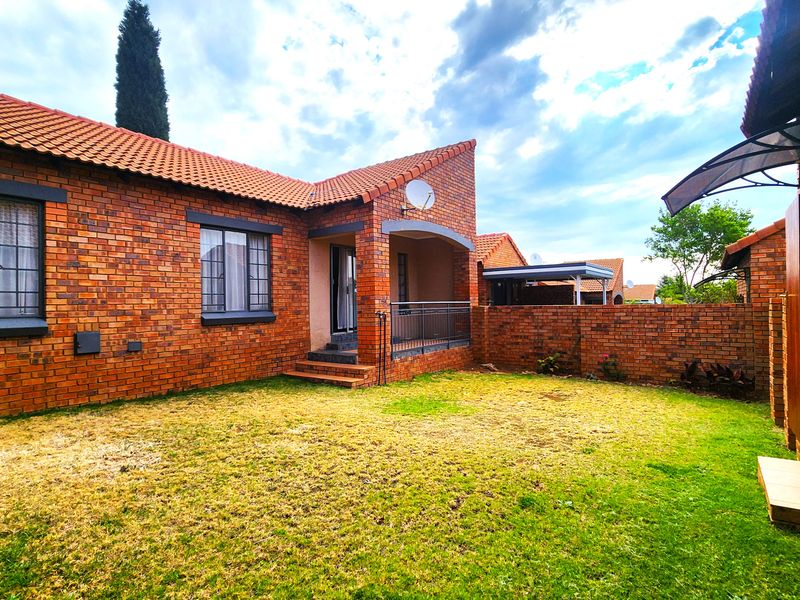 Rear view of a face brick townhouse featuring a small lawn, covered patio area, and secure brick boundary walling.