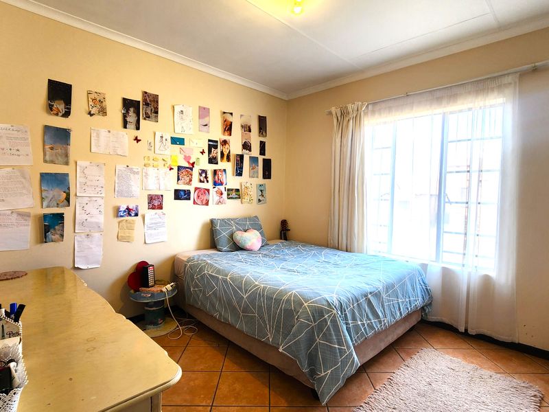 A functional bedroom featuring tiled flooring, a large window with security bars, and neutral wall finishes.