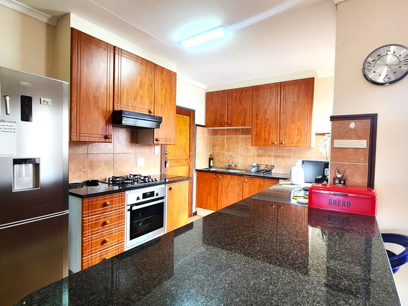 A functional kitchen featuring wooden cabinetry, granite countertops, a gas hob, built-in oven, and a tiled backsplash.
