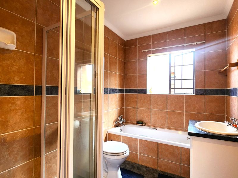 A functional bathroom featuring a shower enclosure, bathtub, vanity with basin, and toilet, finished with full-height wall tiling.