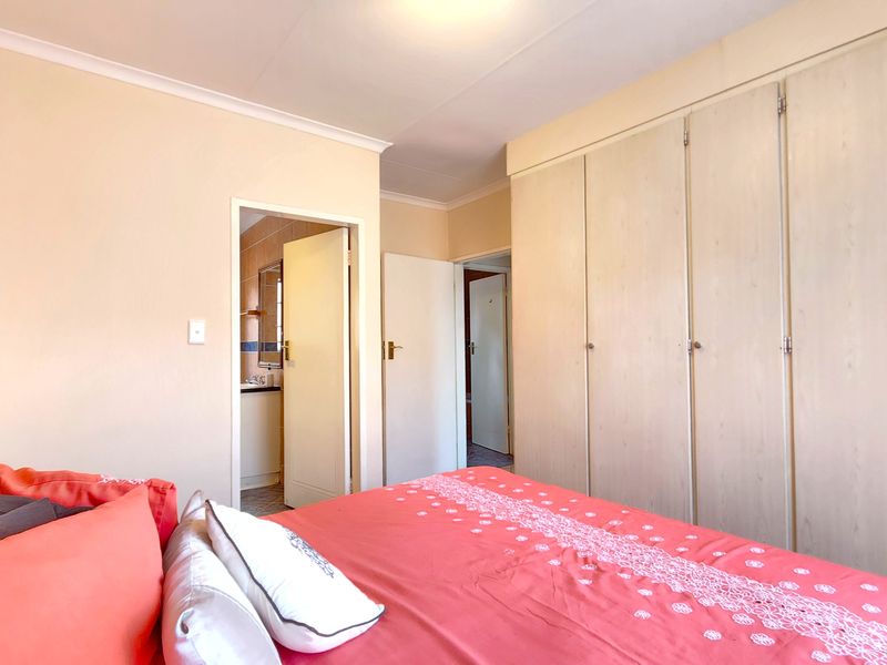 A bedroom featuring built-in cupboards and access to an adjoining bathroom, finished with neutral wall tones and coved cornicing.
