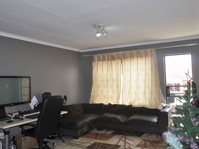 A living room featuring tiled flooring, ceiling coving, and a large window with curtains, providing a functional space for relaxation.