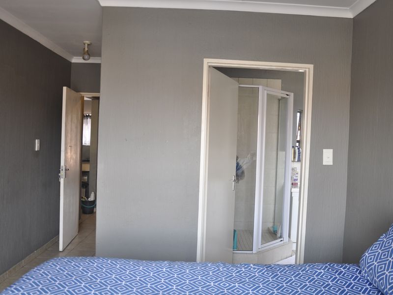 Bedroom featuring an en-suite bathroom with a shower cubicle, neutral grey walls, and tiled flooring.