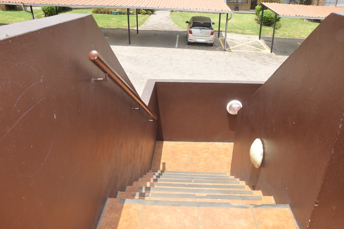 An outdoor staircase with tiled steps and a handrail leading down to a paved parking area with carports.
