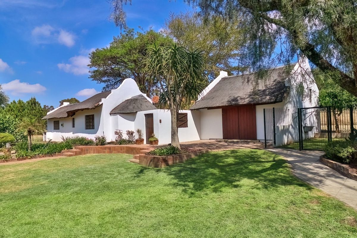 A charming Cape Dutch style cottage featuring a traditional thatched roof, white rendered walls, and a well-maintained garden with brick paved pathways.