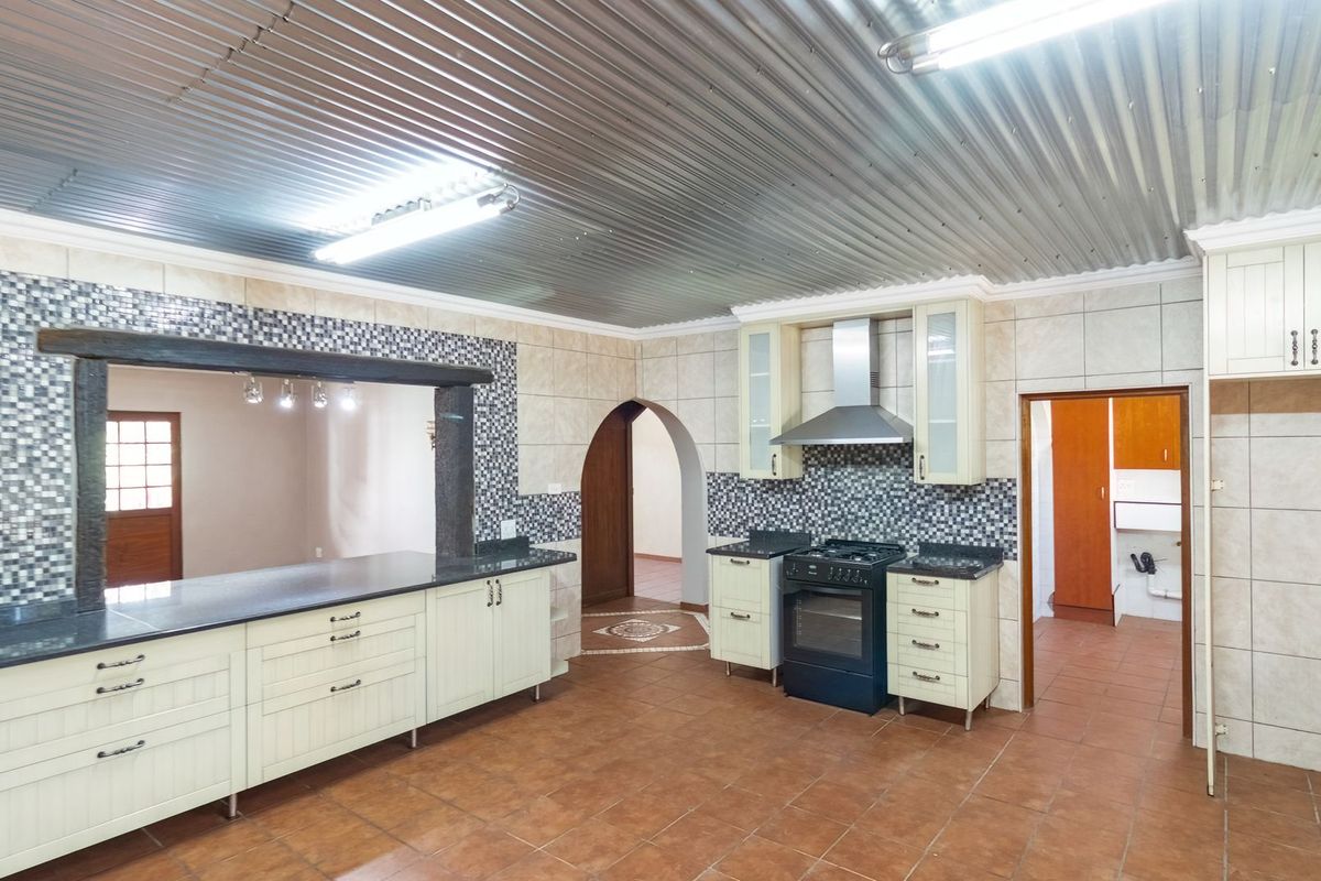 Spacious kitchen featuring built-in cabinetry, granite countertops, a gas stove with extractor fan, and a unique corrugated metal ceiling.