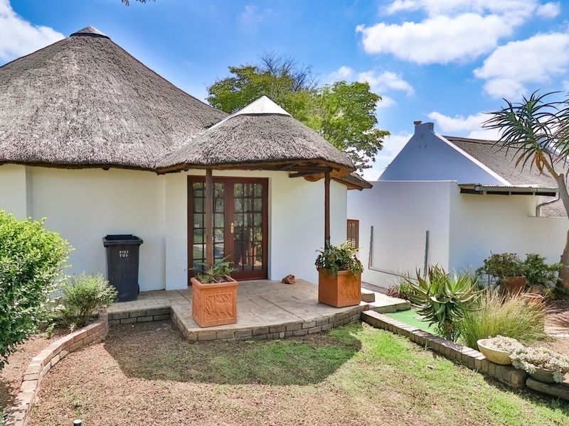 A rear view of a house featuring a traditional thatched roof, a covered patio area, and a landscaped garden with brick-edged beds.