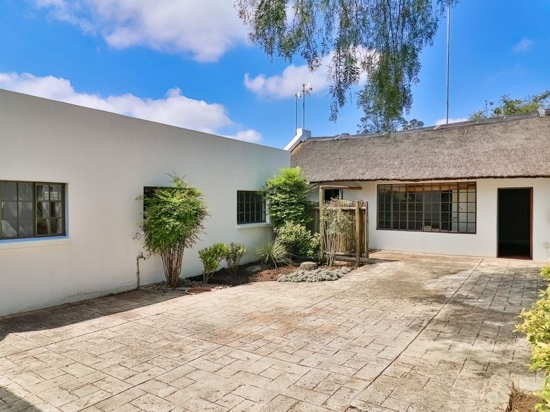 A rear courtyard featuring a paved patio area, traditional thatched roof architecture, and steel-framed windows.