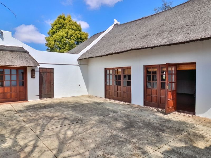 A spacious rear courtyard featuring traditional thatched roofing, white rendered walls, and multiple timber-framed glass doors providing access to the interior living spaces.