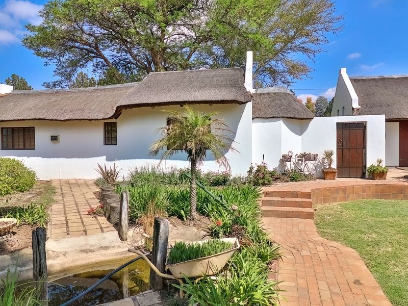 A charming rear exterior view featuring a traditional thatched roof cottage, brick pathways, and landscaped garden area.