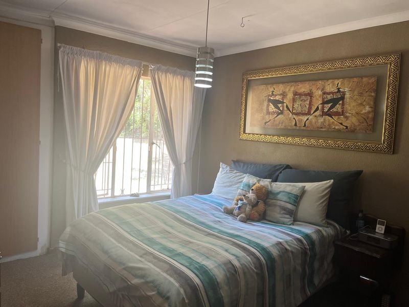 A standard bedroom featuring a built-in cupboard, security bars on the window, and a central pendant light fixture.