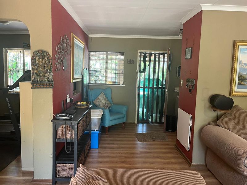 A living area featuring laminate flooring, coved ceilings, and a wall-mounted heater, with direct access to the exterior through a security gate.