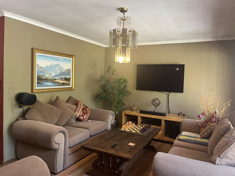 A comfortable living room featuring laminate flooring, coving, and a decorative crystal chandelier, providing a functional and inviting space for relaxation.