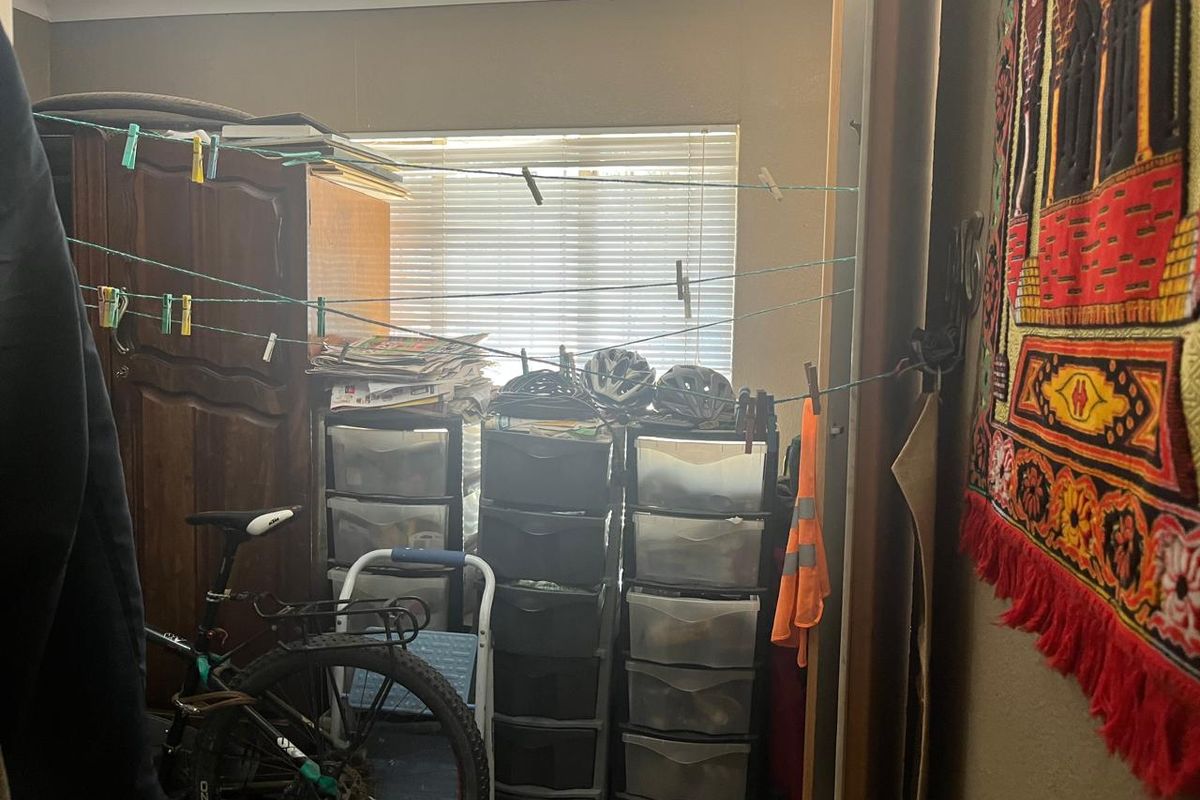 A bedroom space featuring a built-in cupboard and window with venetian blinds, currently utilized for storage.