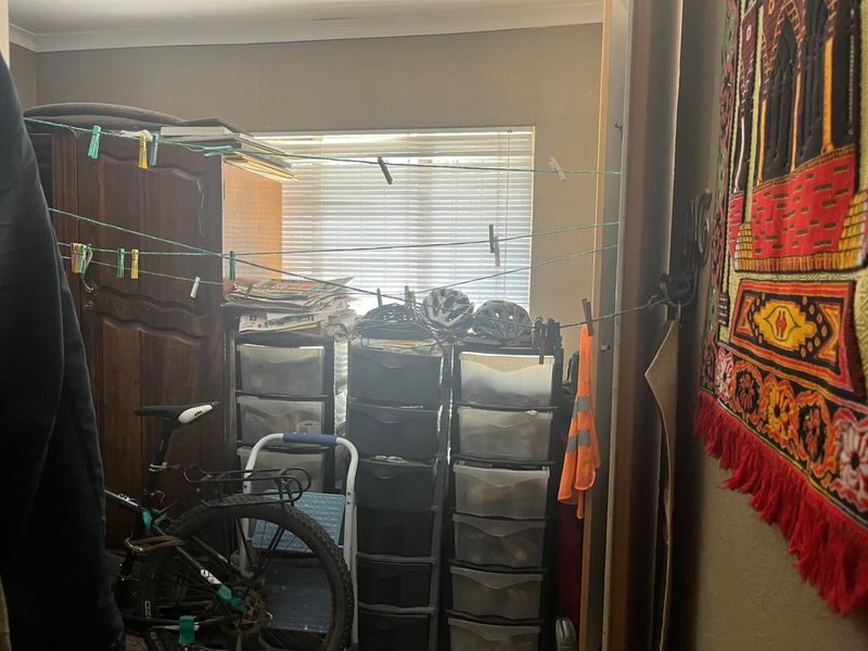 A bedroom space featuring a built-in cupboard and window with venetian blinds, currently utilized for storage.