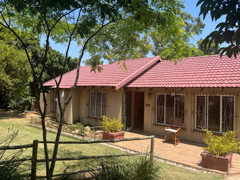 Front elevation of a single-story house featuring a tiled roof, security bars on windows, and a paved patio area overlooking a landscaped garden.