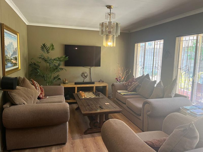 A comfortable living room featuring laminate flooring, decorative cove cornicing, and a classic crystal chandelier, with security bars fitted to the windows.